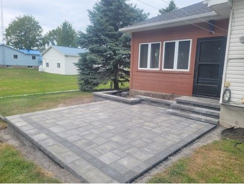 Brick patio next to a house with a red wall and a door, steps, and a green lawn.