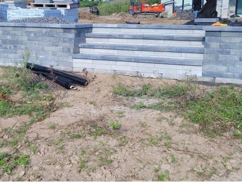 Marches en briques grises et mur de soutènement en construction sur un terrain en terre.