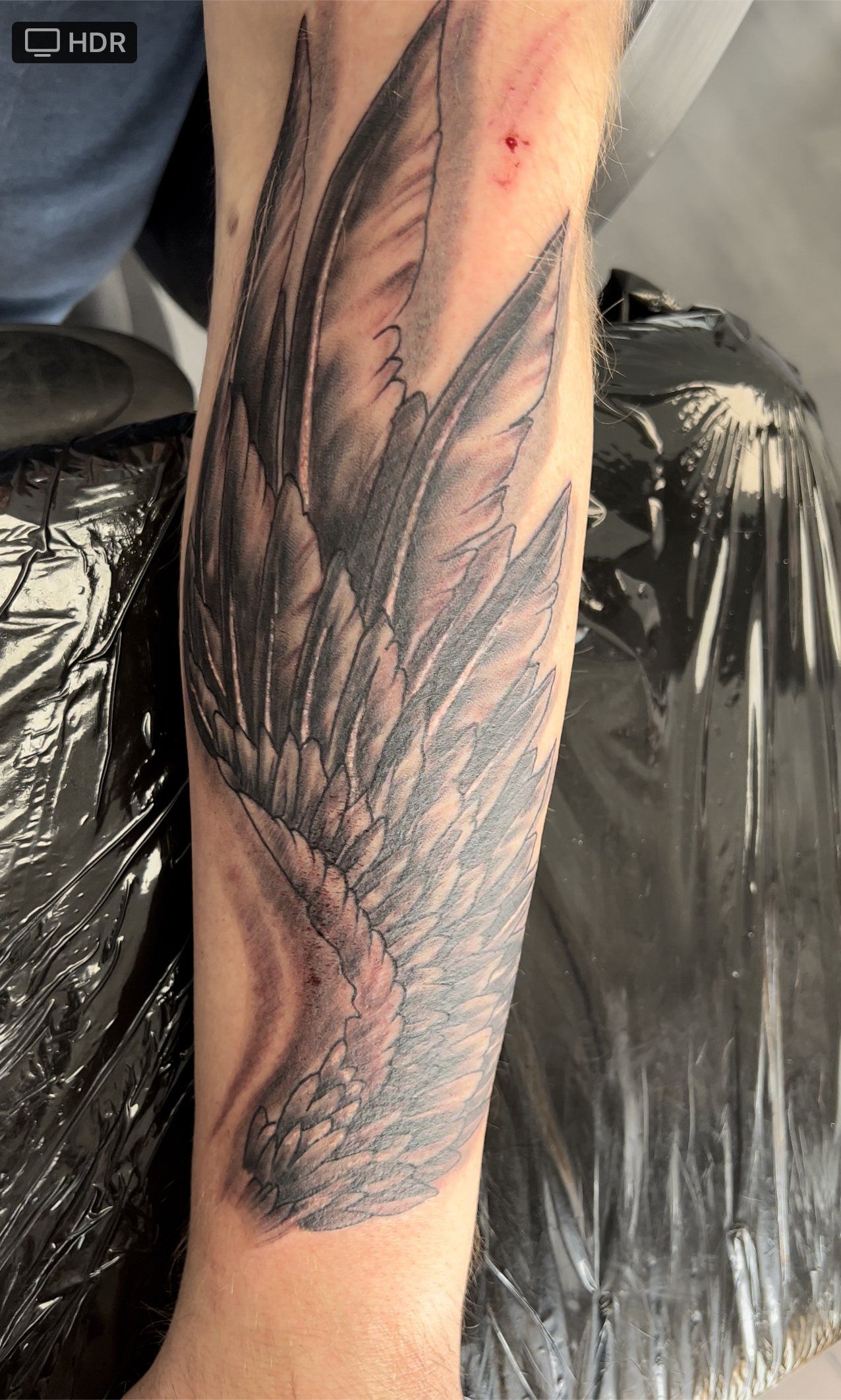 Eine Person hat eine Tätowierung mit Vogelflügeln auf ihrem Unterarm.