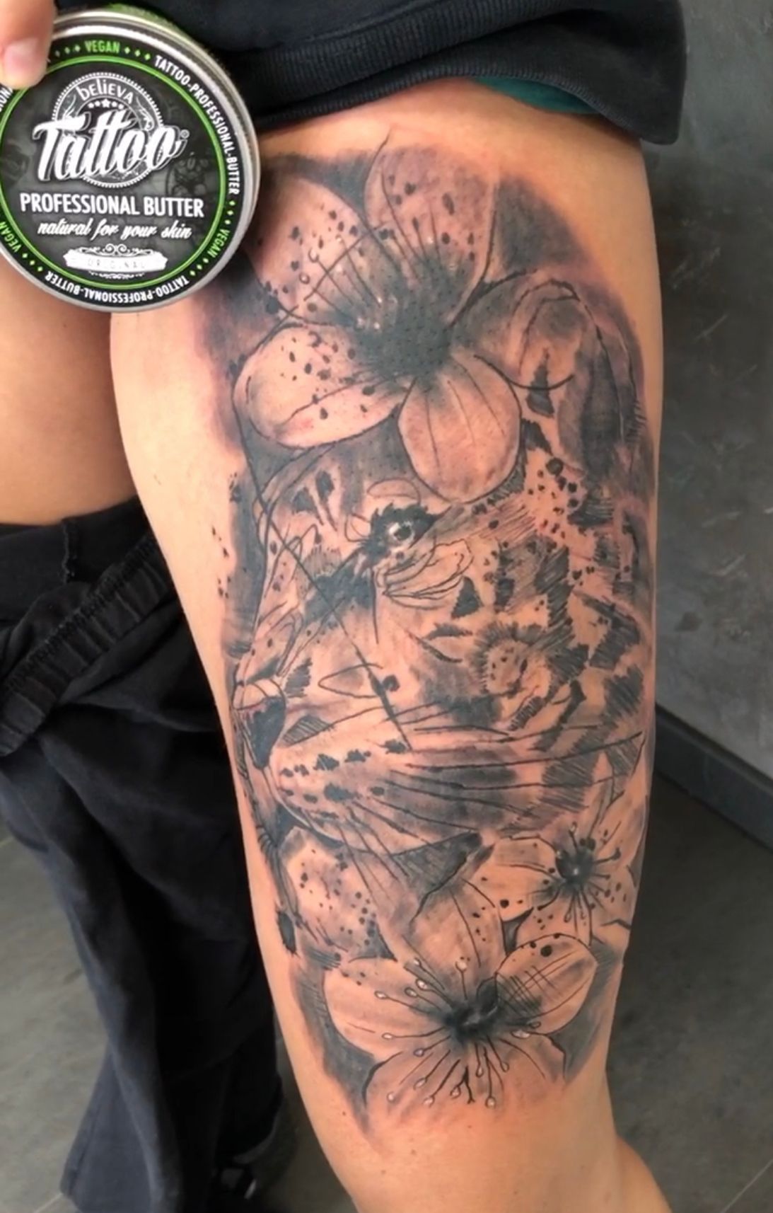 Eine Frau hat ein Tattoo mit einem Löwen und Blumen auf ihrem Bein.