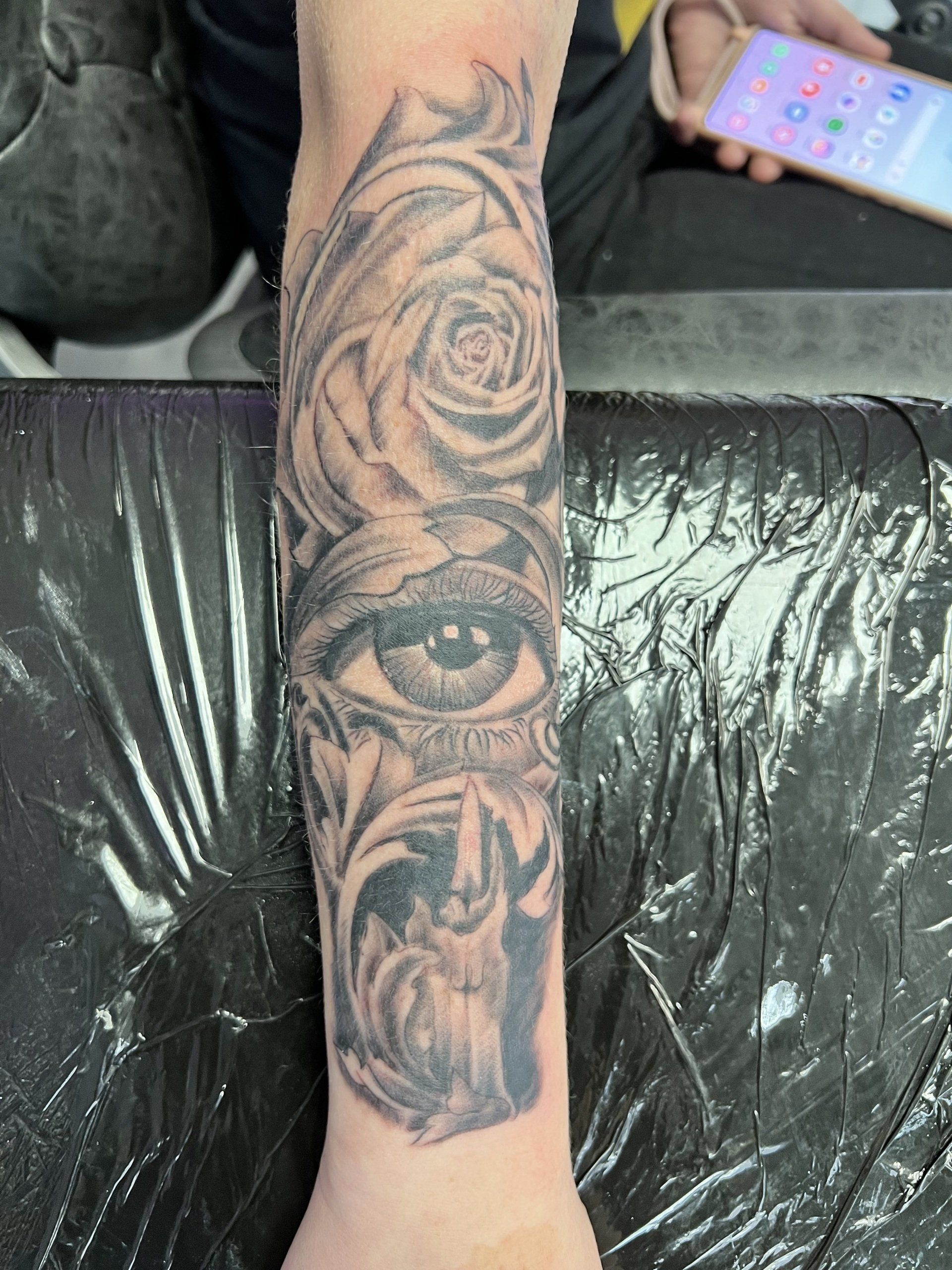 Eine Person hat eine Tätowierung mit einem Auge und Rosen auf dem Unterarm.