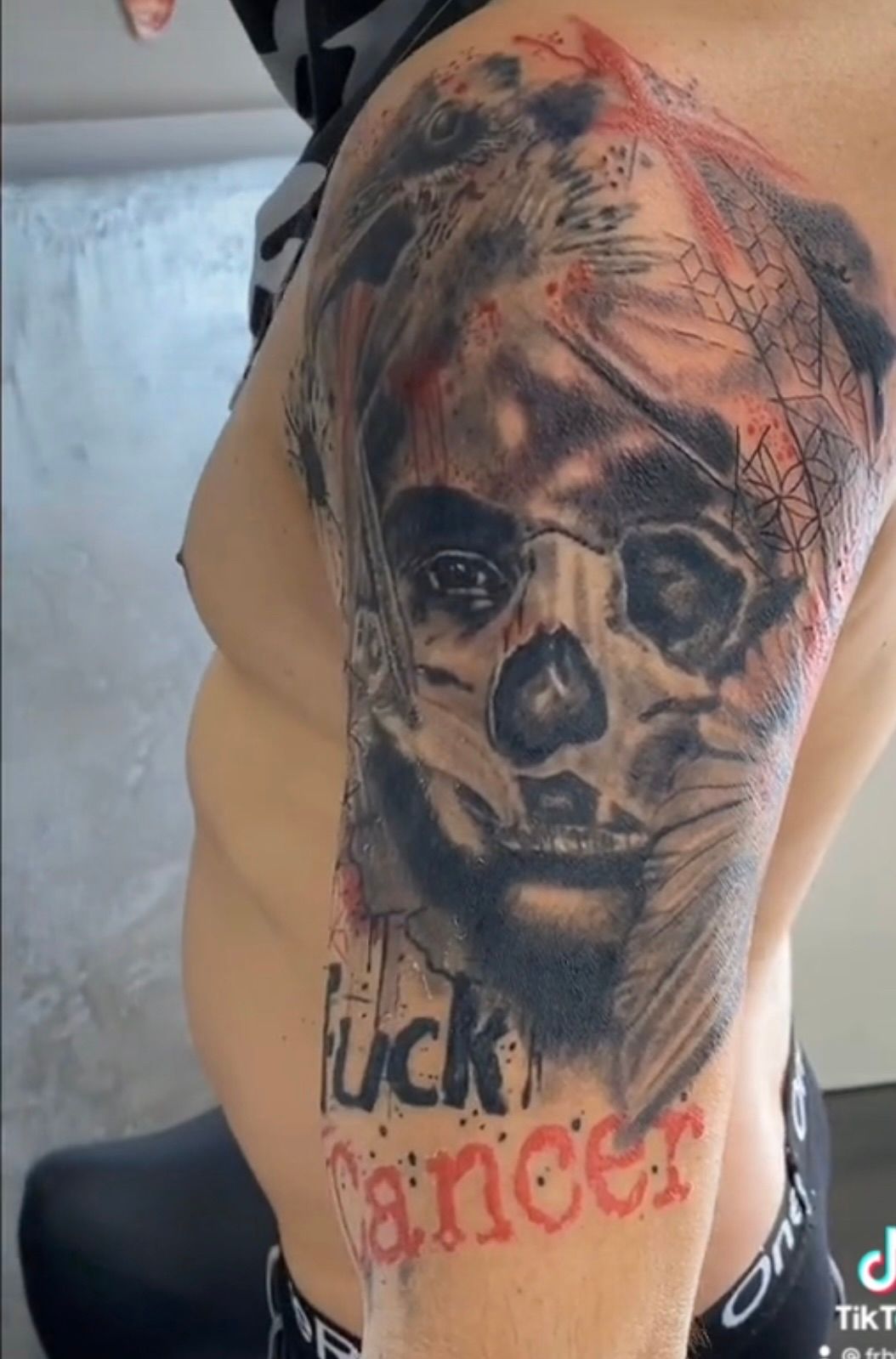 Ein Mann hat ein Tattoo mit einem Totenkopf und dem Wort Krebs auf seinem Arm