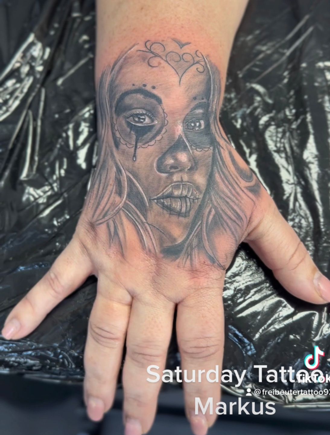 Eine Hand mit einem Tattoo eines Frauengesichts darauf