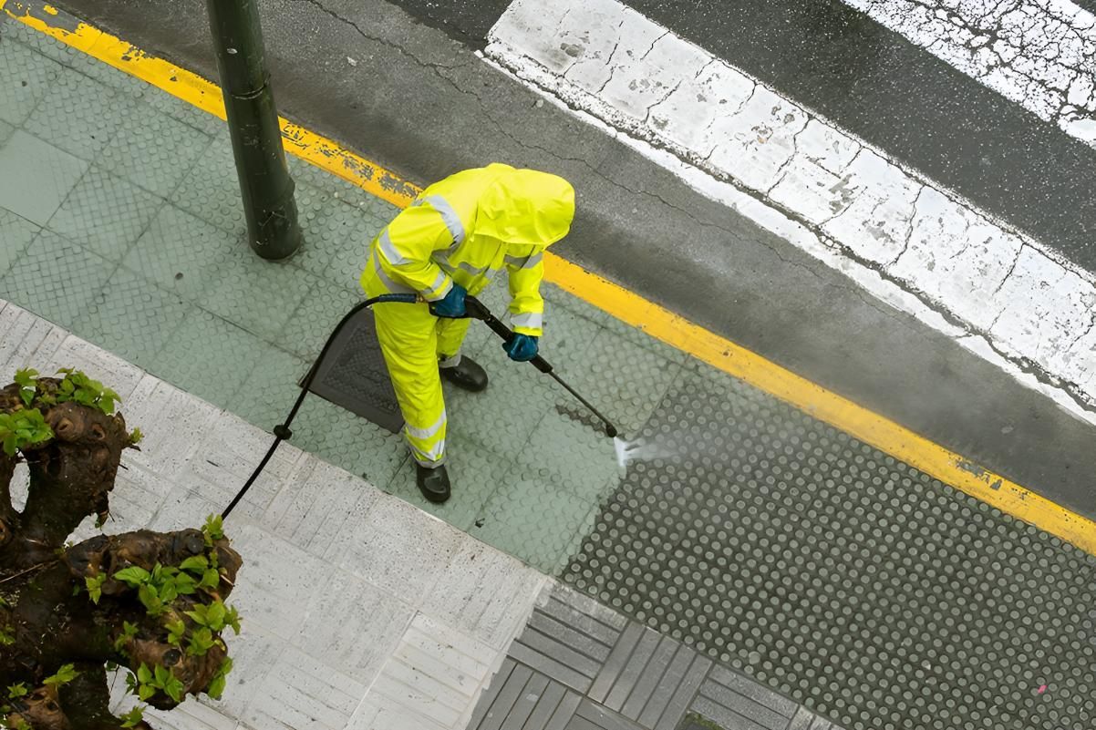 A Man in a Yellow Suit is Cleaning the Sidewalk With a High Pressure Washer — Porta-Vac in Proserpine, QLD