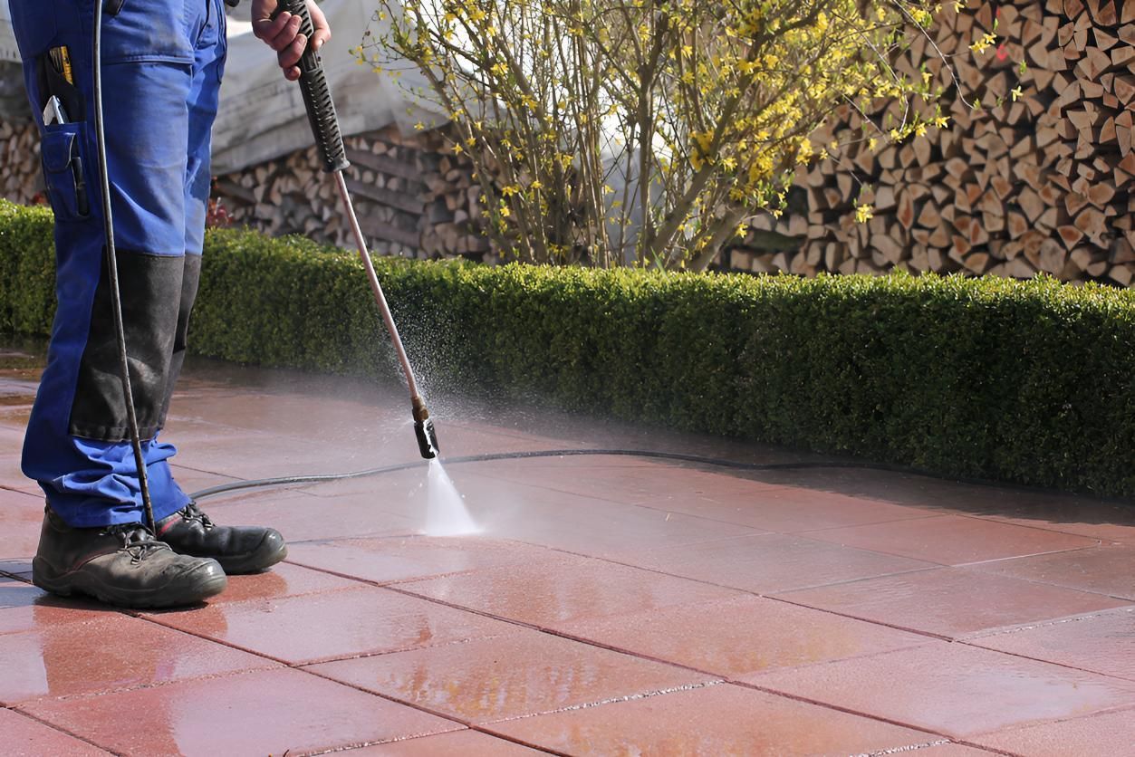 A Man Is Using A High Pressure Washer To Clean A Patio — Porta-Vac in Bowen, QLD