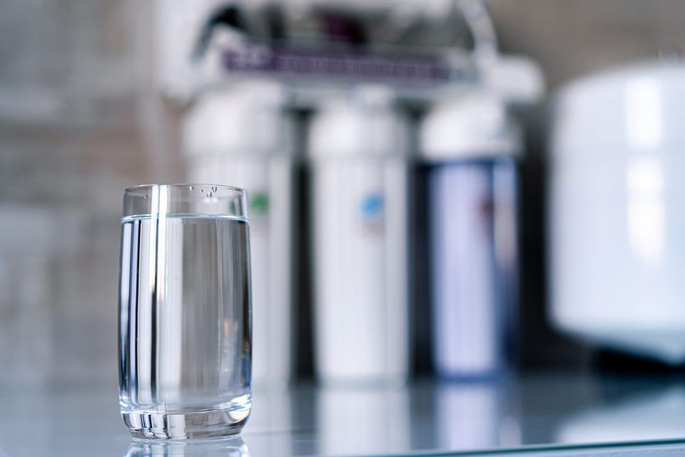A Glass Of Water Sits On A Table Near A Water Filter — Porta-Vac in Proserpine, QLD