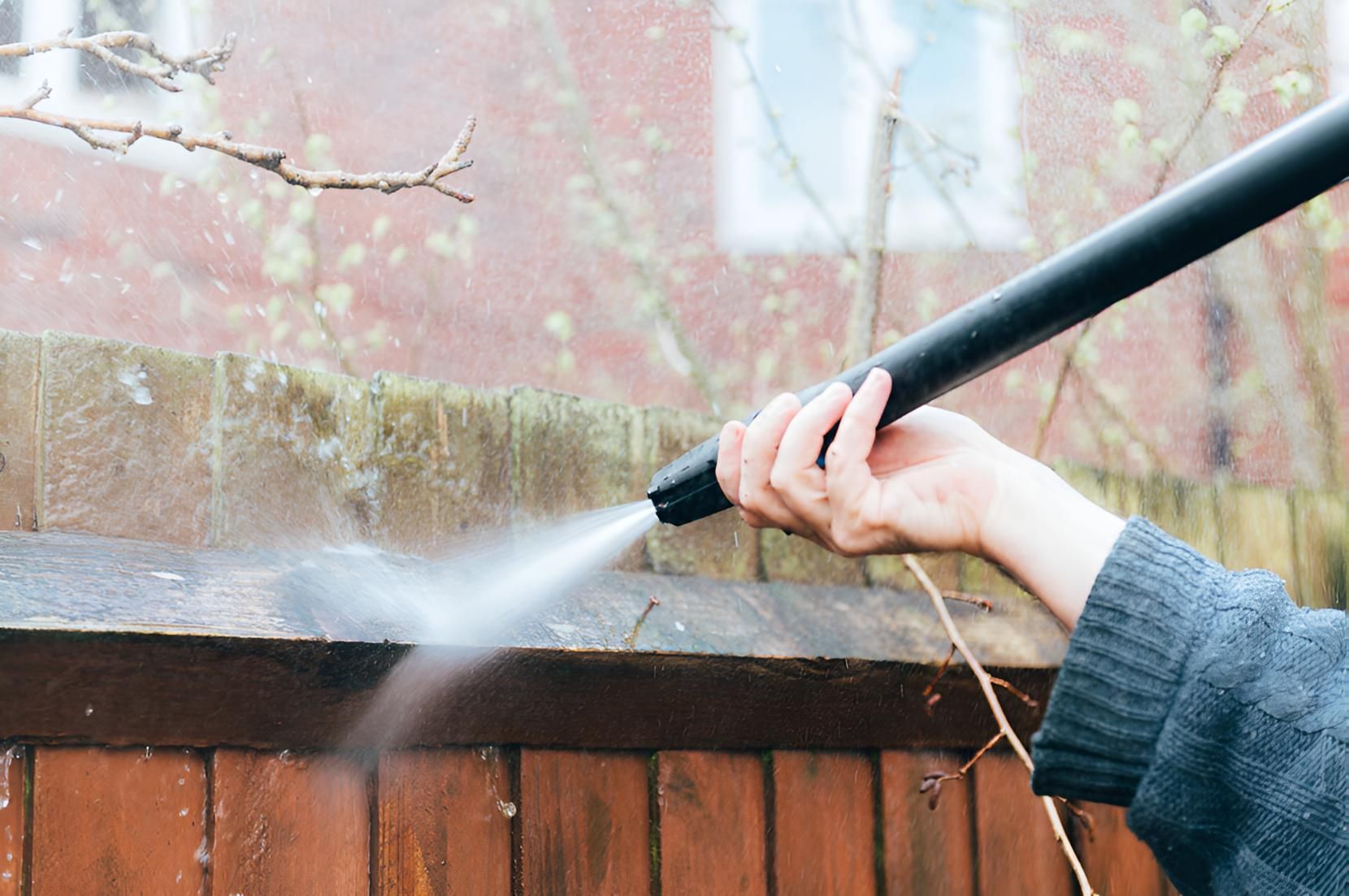 A Person Is Using A High Pressure Washer To Clean A Wooden Fence — Porta-Vac in Cannonvale, QLD