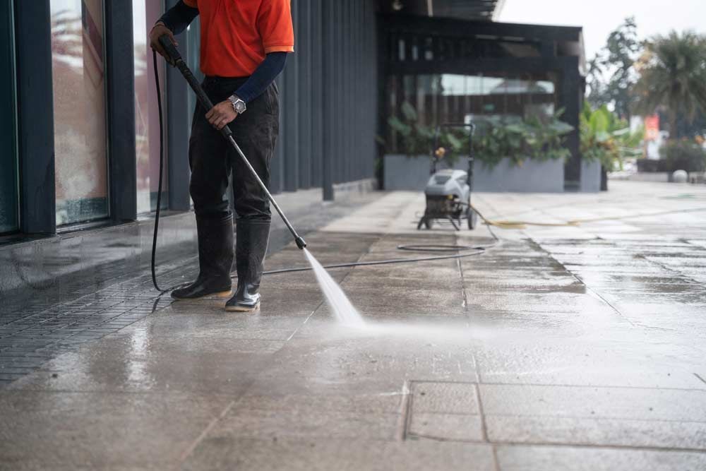 Worker Hoses A Portable Washing The Concrete Floor With High-pressure Water Jets — Porta-Vac in Airlie Beach, QLD