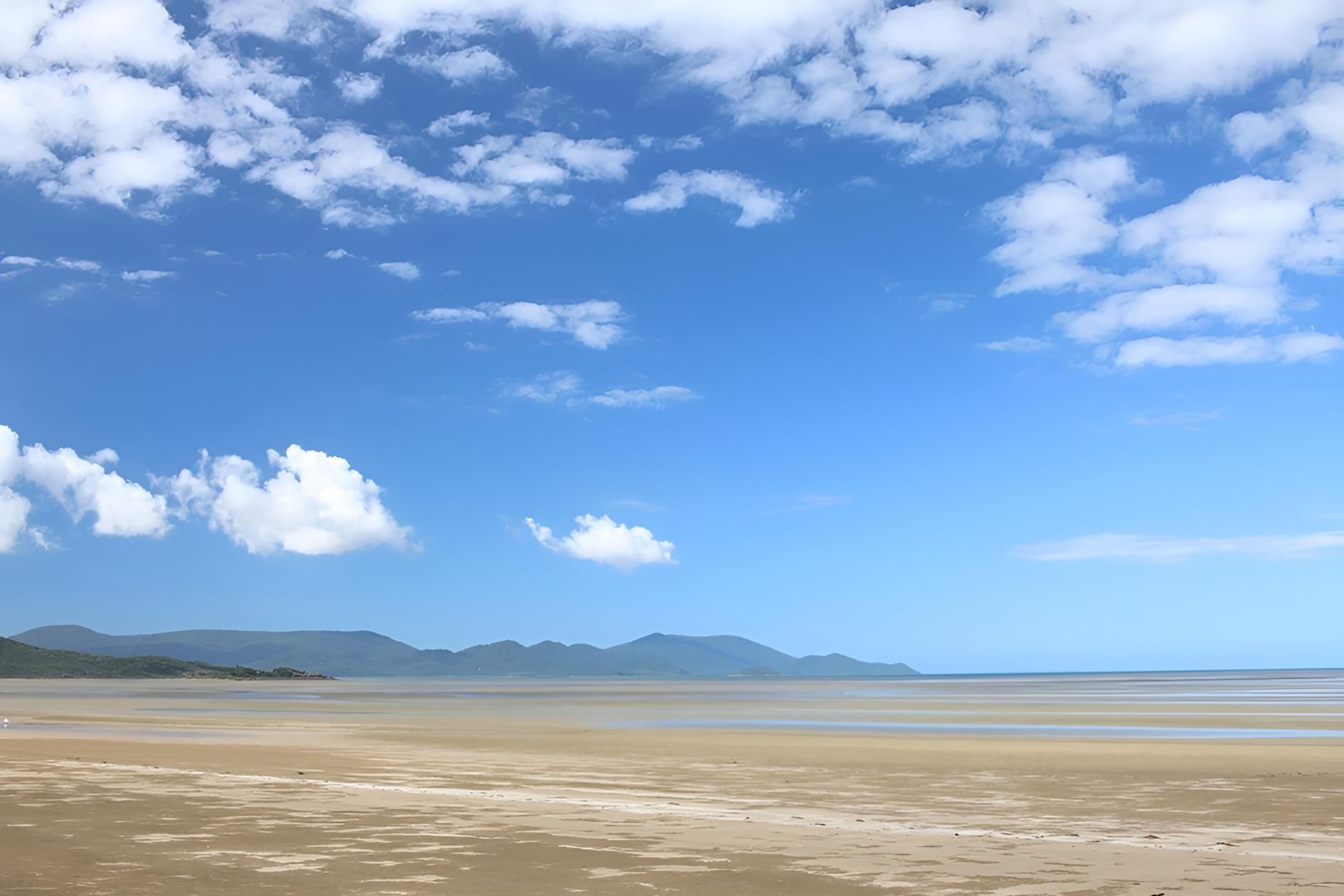 A Beach With Mountains In The Background And A Blue Sky With Clouds — Porta-Vac in Cannonvale, QLD