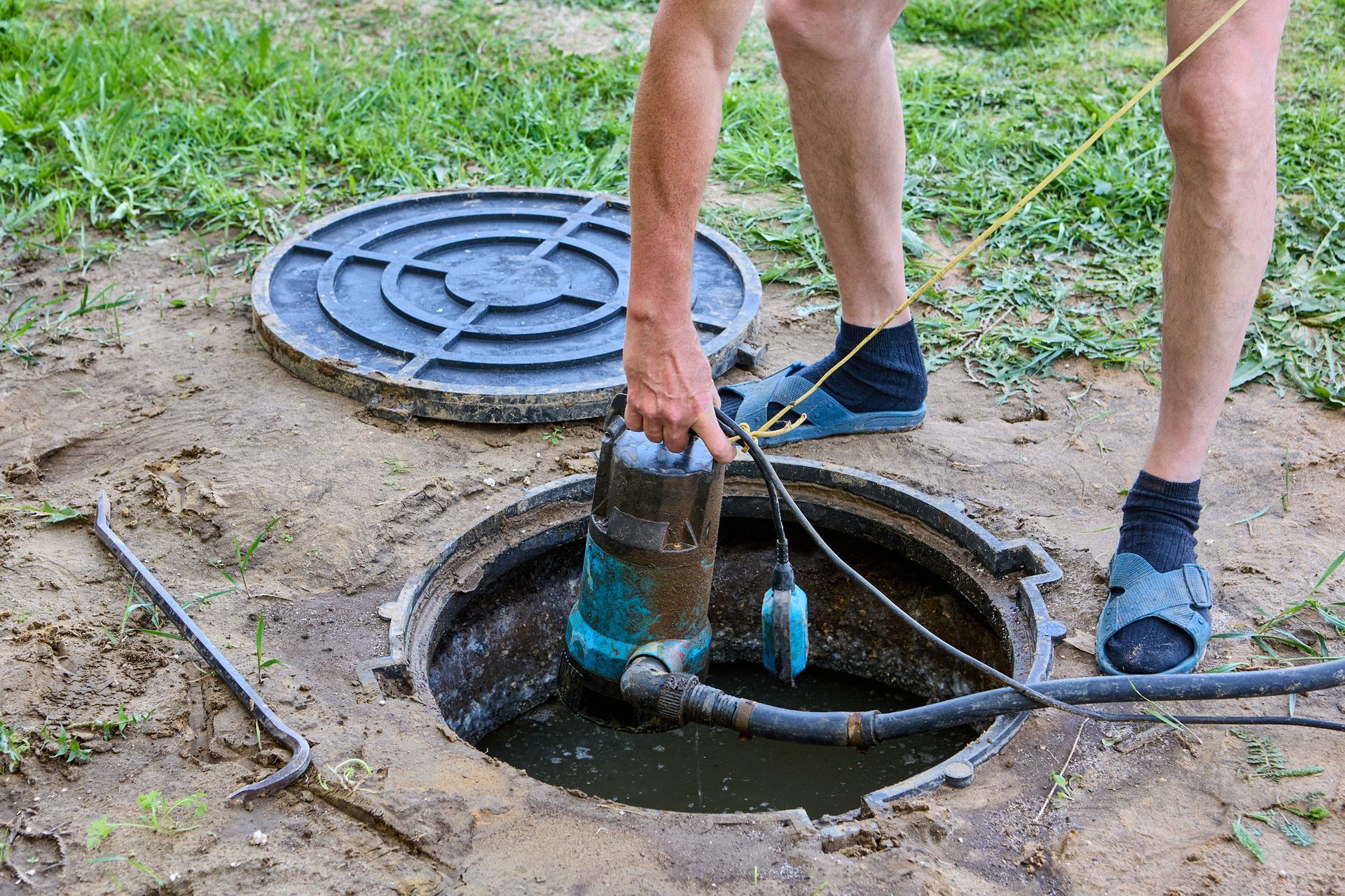 Worker removing submersible pump from septic tank during affordable septic service maintenance.