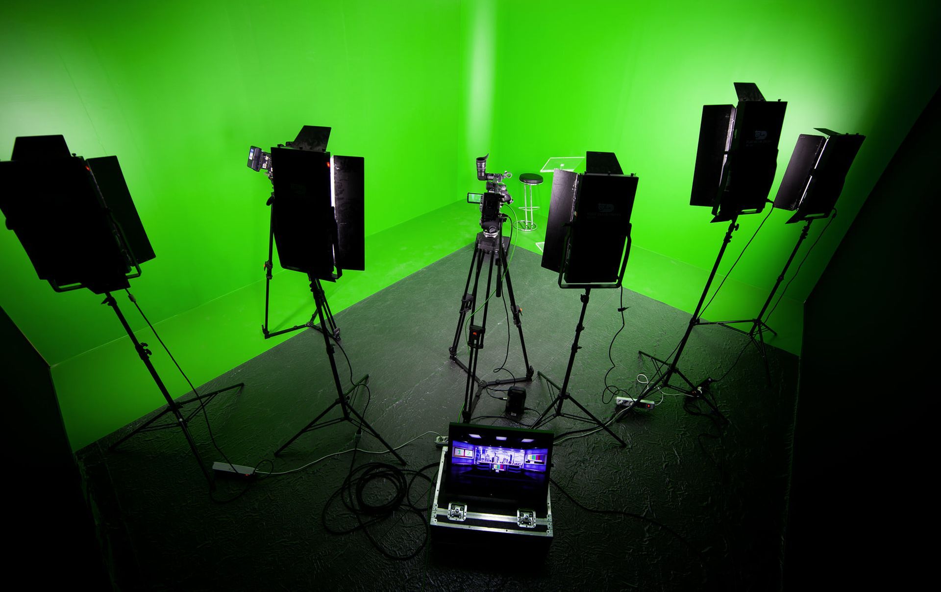 Studio con schermo verde allestito con telecamera su treppiede, luci e monitor.