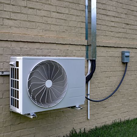 A white fan is attached to the side of a brick building
