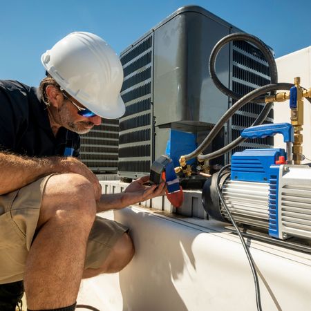 A man wearing a hard hat is working on an air conditioner