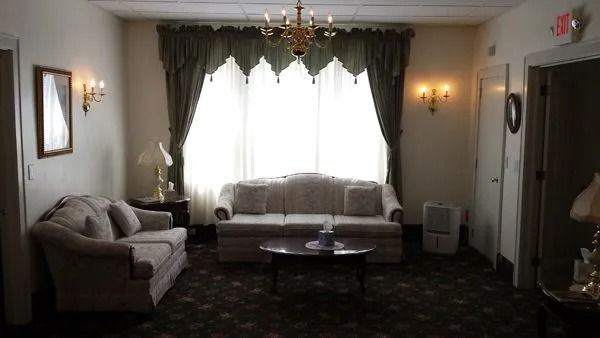 A room with couches, a window with curtains, a chandelier, and wall sconces.