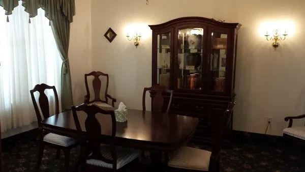 Dining room with dark wooden table and chairs, display cabinet, and sconces on a white wall.