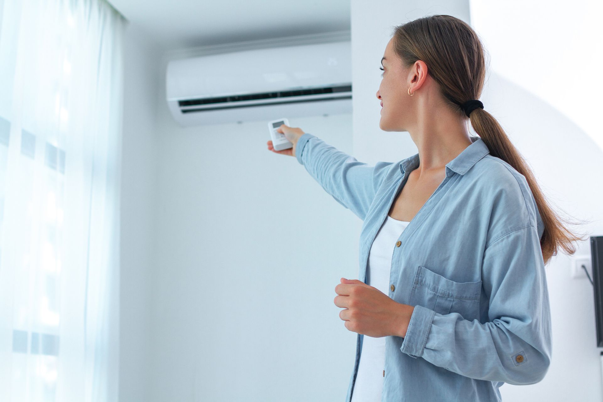 A young woman adjusts the temperature of the air conditioner. A young woman adjusts the temperature of the air conditioner.