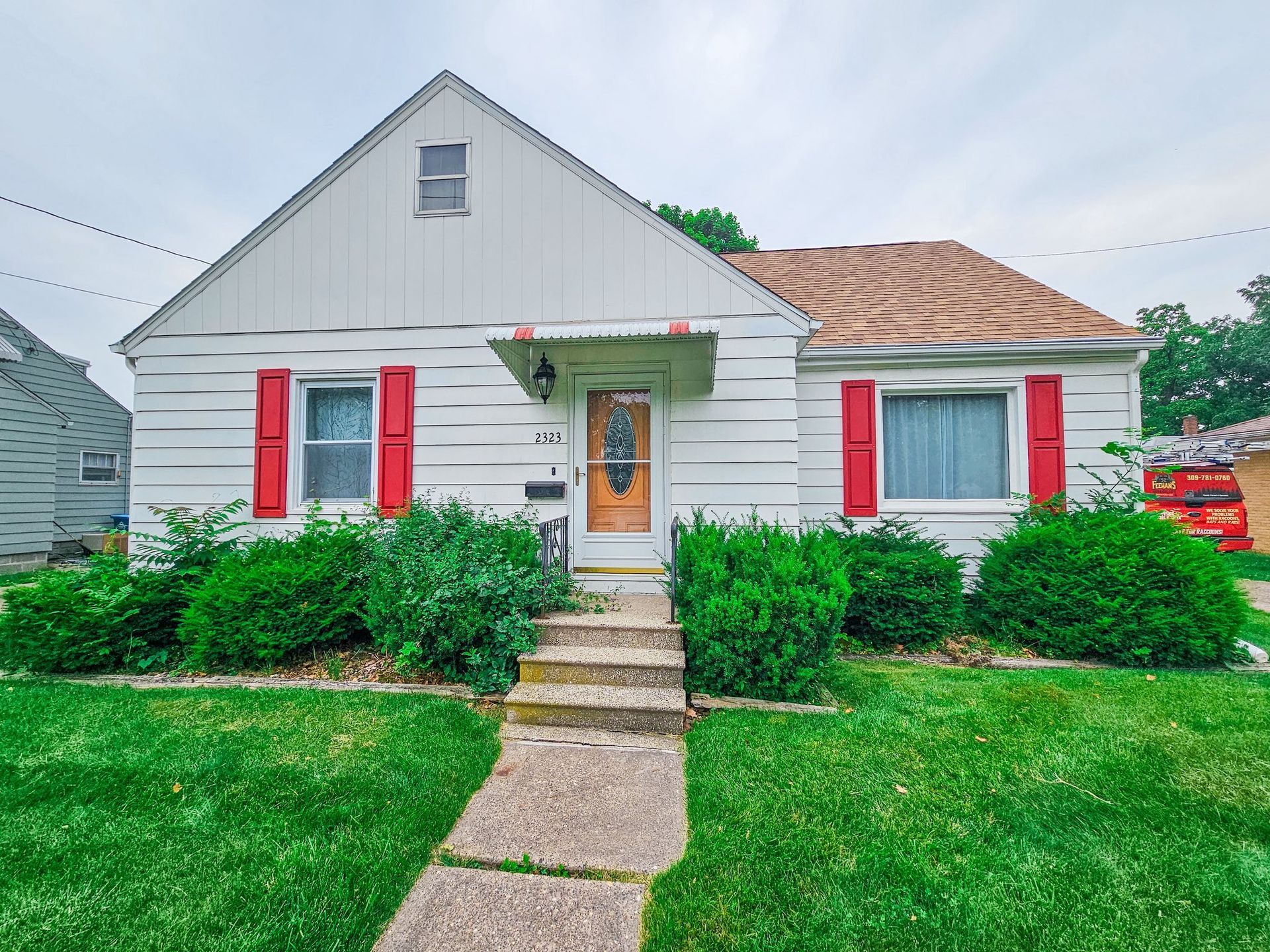 A one-story house with white horizontal siding, a gabled roof, red window shutters, and a concrete front walkway.
