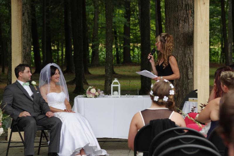 Les mariés sont assis à une table tandis qu’une femme tient un microphone.