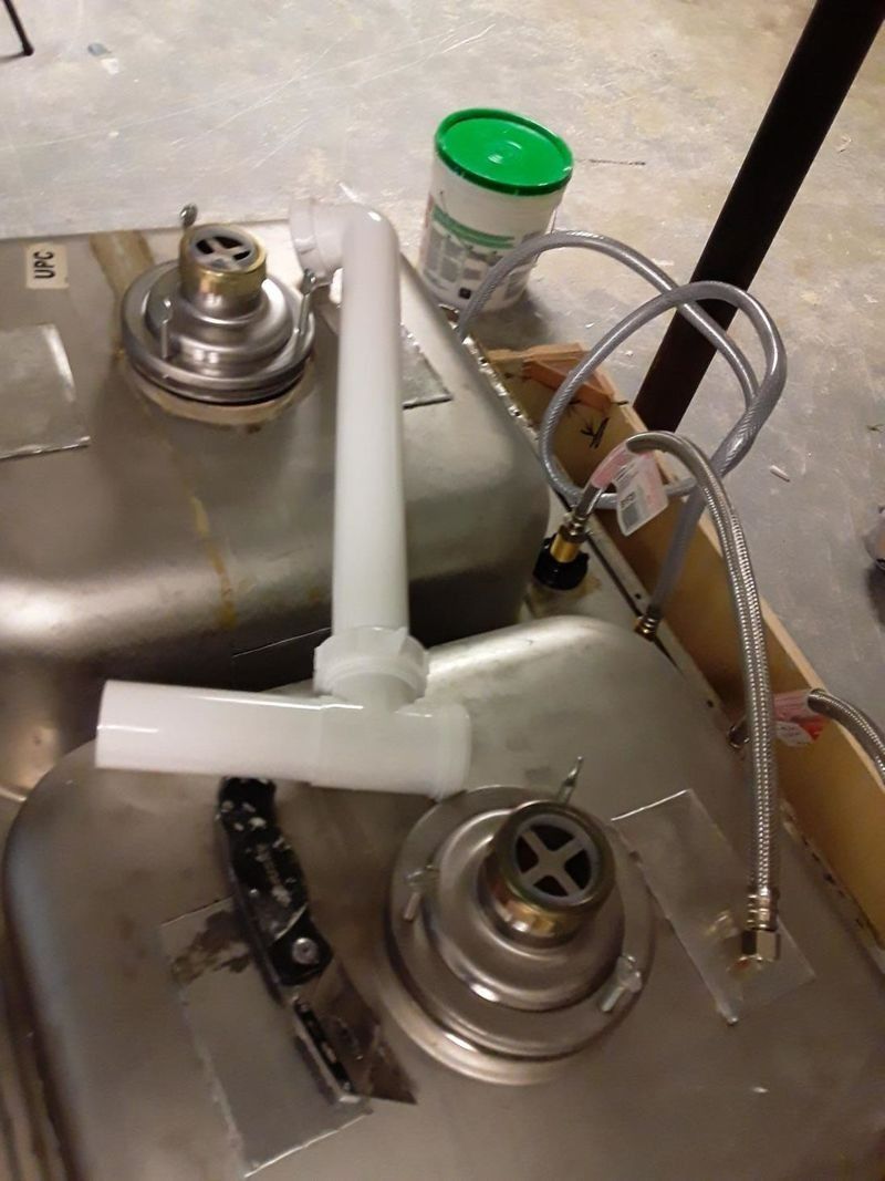 Stainless steel kitchen sink with plumbing parts, including a drain, pipe, and water lines.