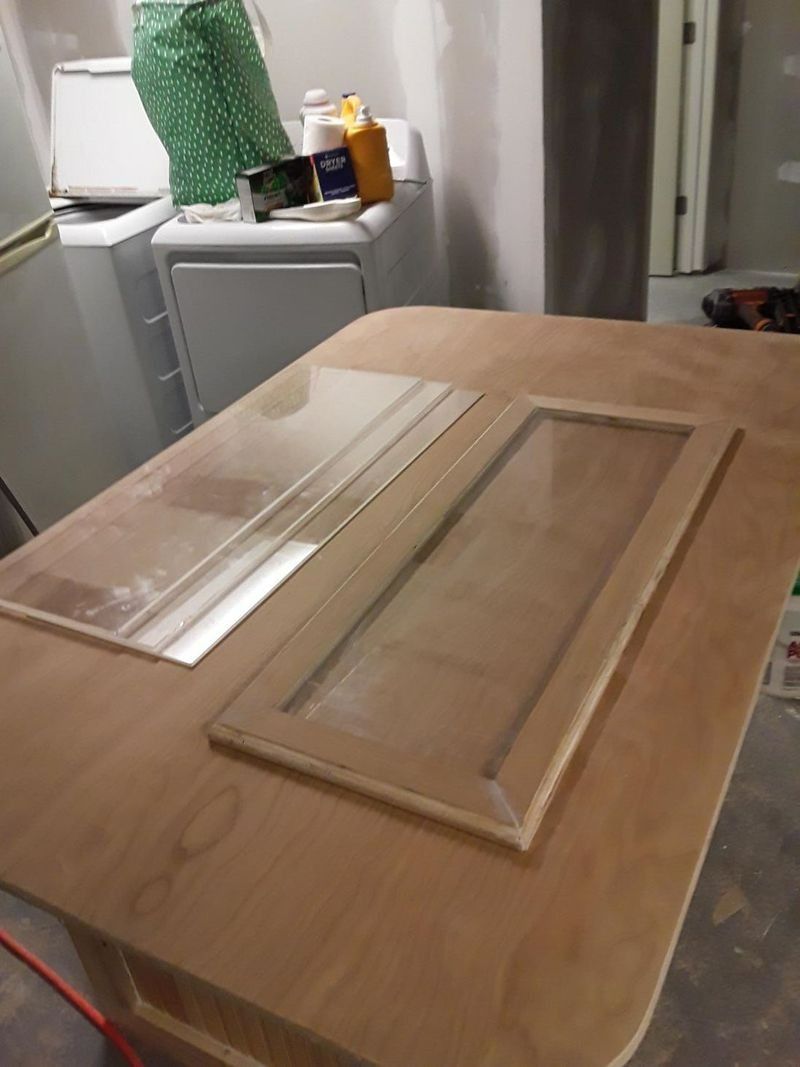 Two cabinet doors with glass panes sit on a light wood table in a room.