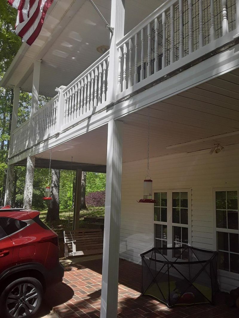 Red SUV parked beneath a white two-story porch. American flag, bird feeder, and swing visible.