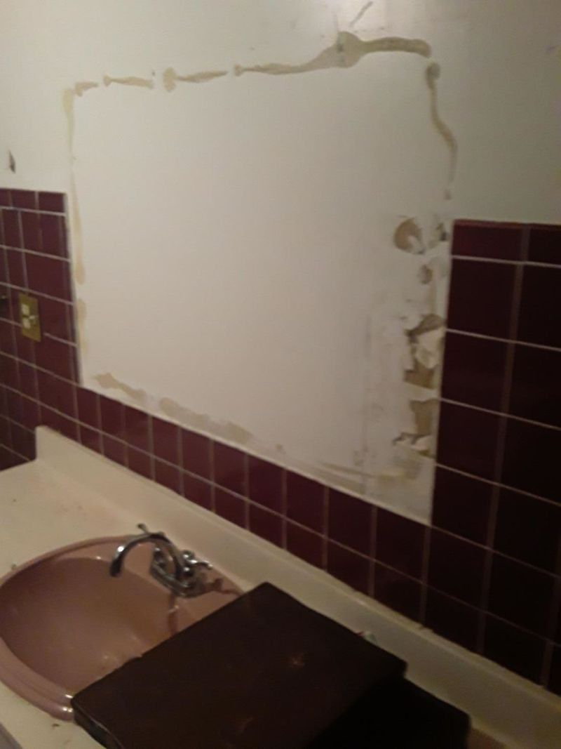 Bathroom with pink sink, maroon tiles, and a section of wall with damaged paint.