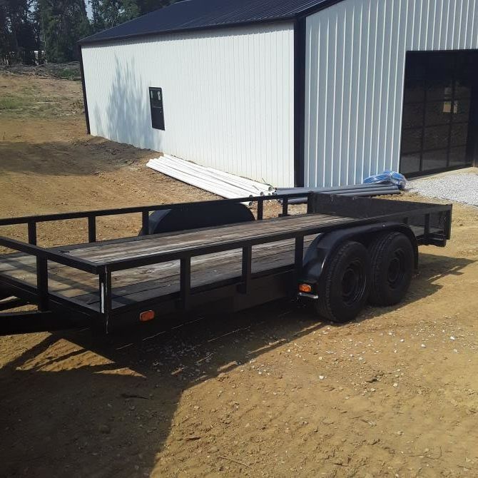 Black utility trailer parked in front of a white metal building with black roof.