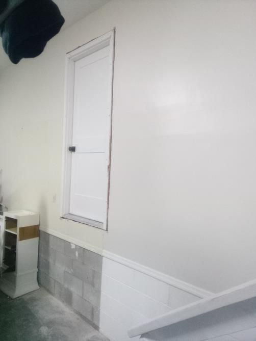 White door in a white wall above a gray cinder block foundation.