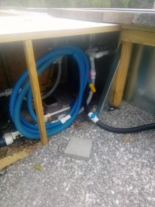 Blue coiled tubing and white PVC pipes under a wooden structure on a gravel surface.