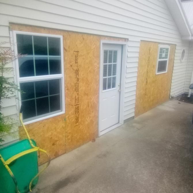 Exterior of a building with a window, door, and a small window surrounded by plywood.