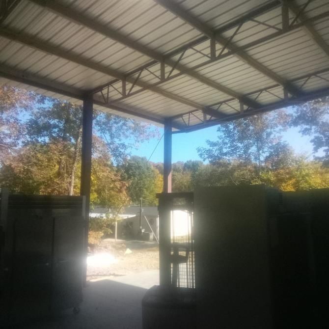 Open-air metal-roofed structure; trees with fall foliage in background.