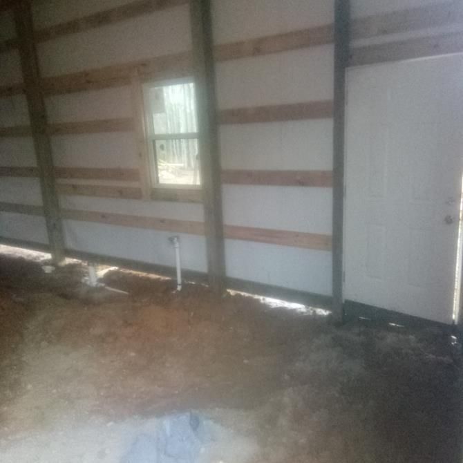 Interior of a partially constructed building. Wooden beams frame the walls, white panels, door, and a small window.