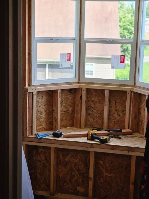 Bay window interior under construction, wood frame and OSB panels installed. Tools on the built-in bench.