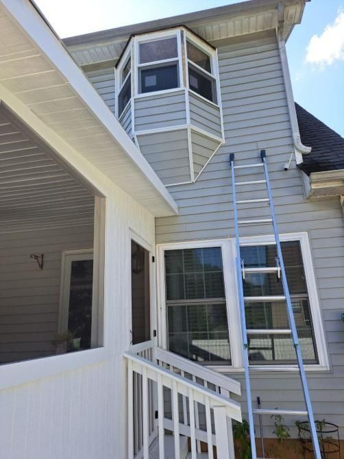 House exterior with bay windows and a ladder leaning against it. White porch visible.