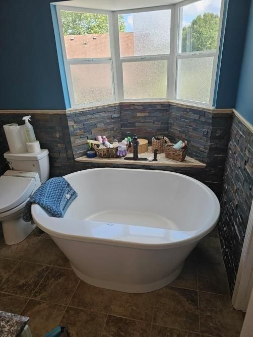 Bathroom with a white oval bathtub, stone accent wall, blue walls, and a large window.