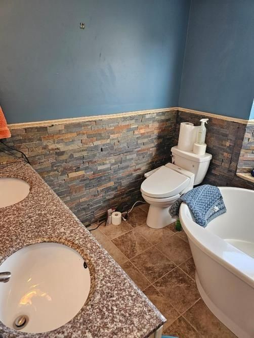 Bathroom with dual sinks, a toilet, a bathtub, and stone accent wall.