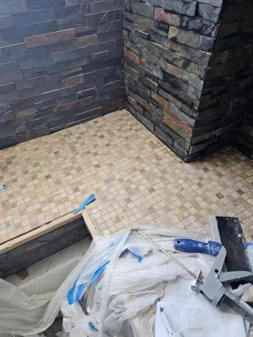 Shower stall with textured stone walls and tiled floor, construction in progress.
