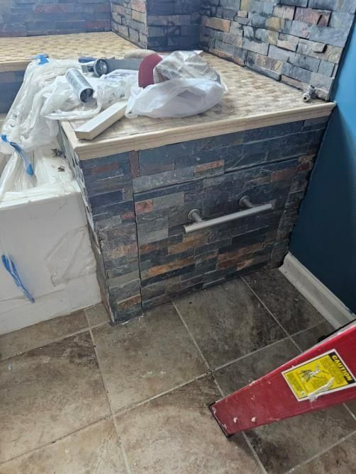 Bathroom cabinet with stone veneer, silver handle, tan countertop, and brown tile floor.