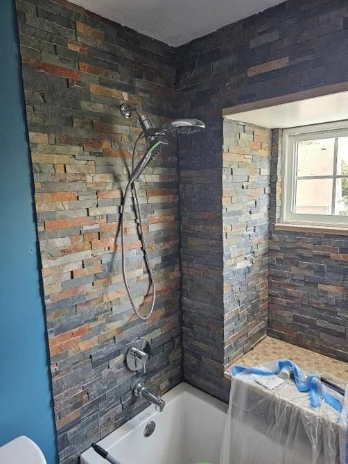 Shower with stone tile walls, showerhead and fixtures. Blue wall and a window visible.