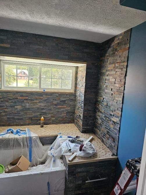 Bathroom with stone tile walls, a window, and a partially finished bathtub area. Blue accent wall visible.