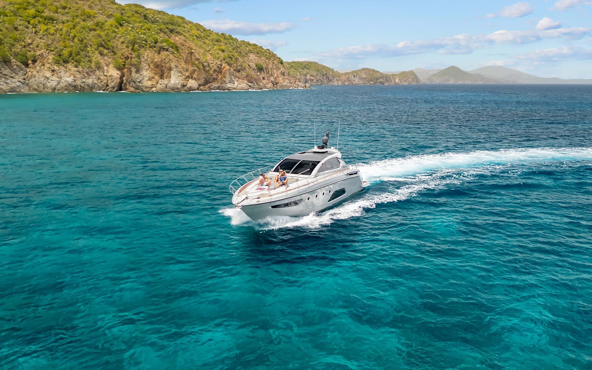 White motor yacht speeding across turquoise water near a lush, green shoreline.