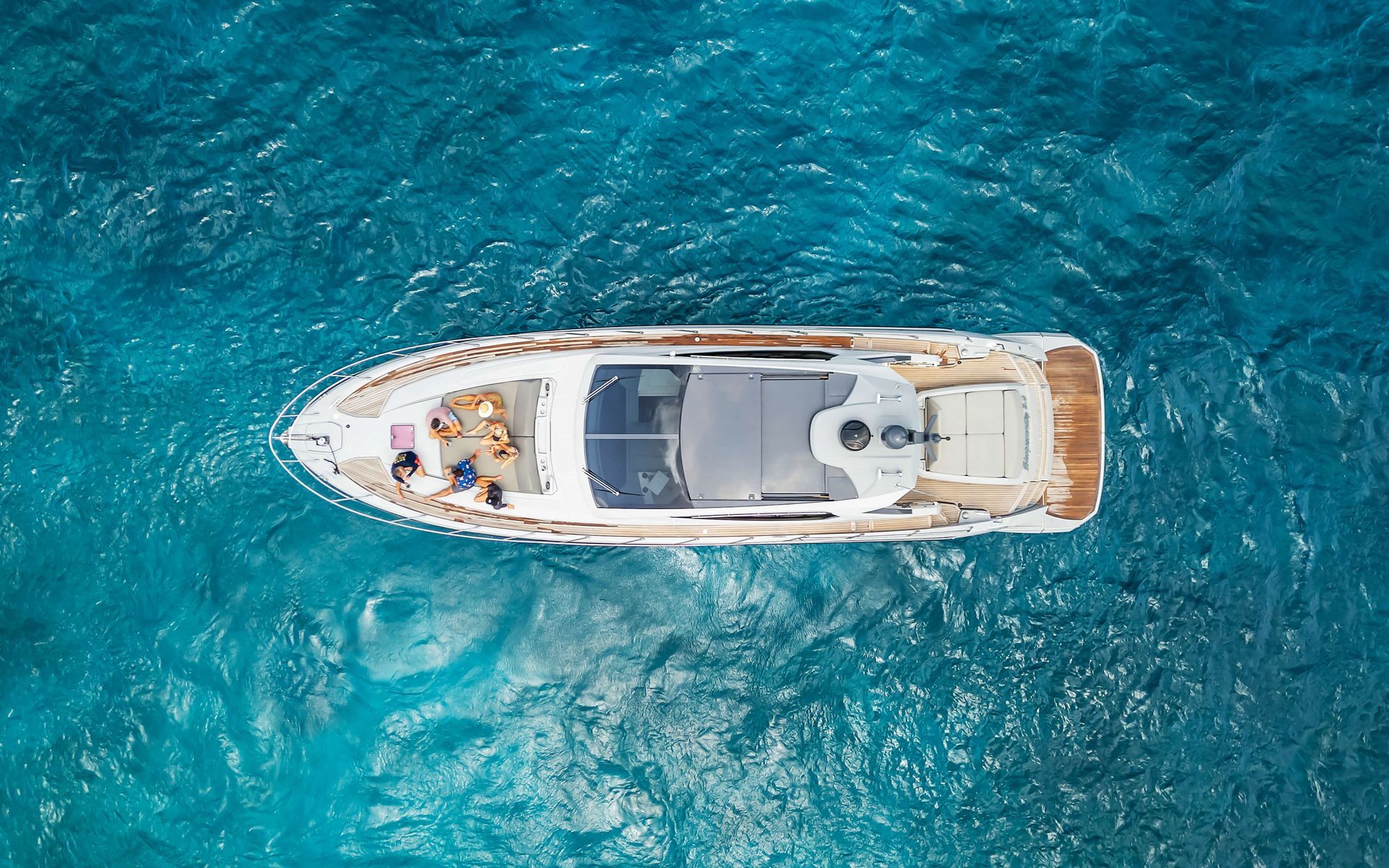 Overhead view of a white yacht on turquoise water, people relaxing on deck.