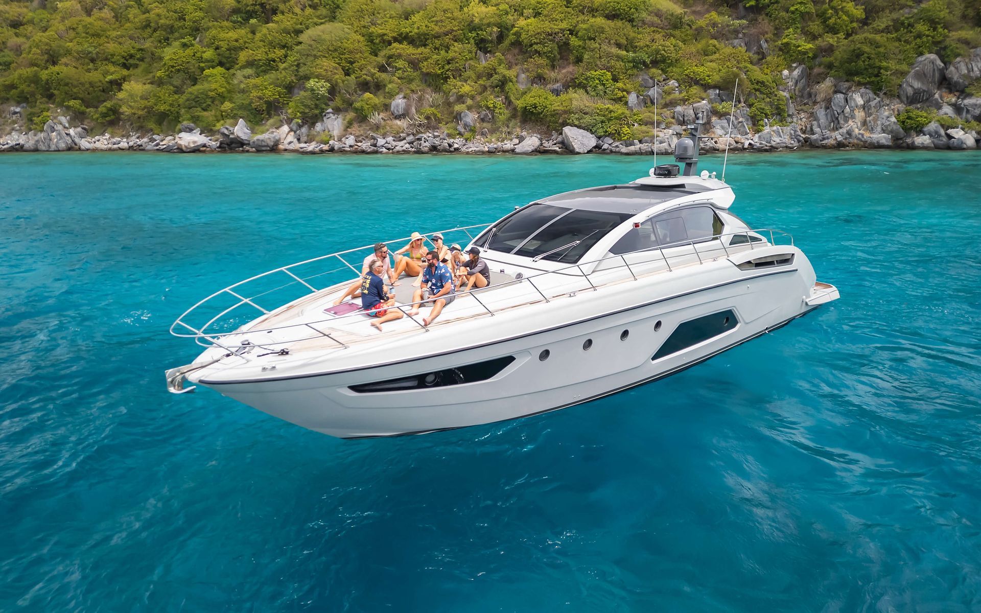 White yacht with group sunbathing on deck in turquoise water.