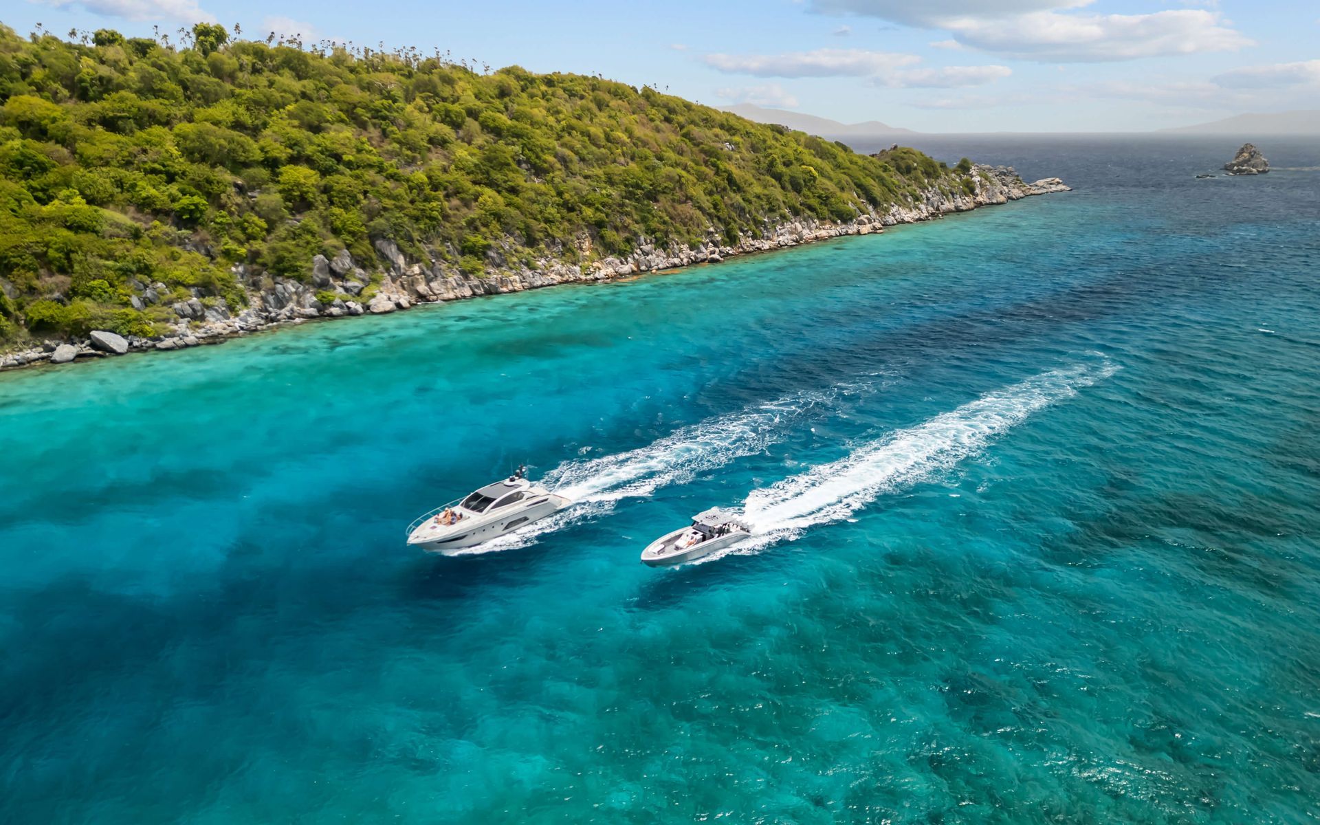 Two motorboats speeding on turquoise water near a lush, green shoreline.