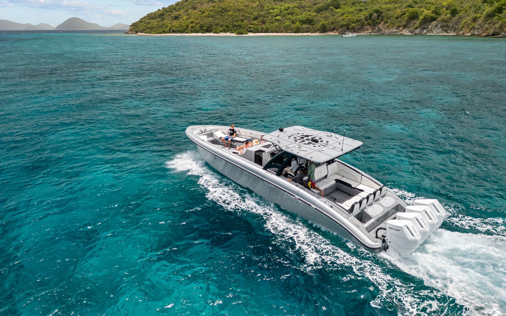 A gray motorboat speeds through turquoise water near a lush green island.