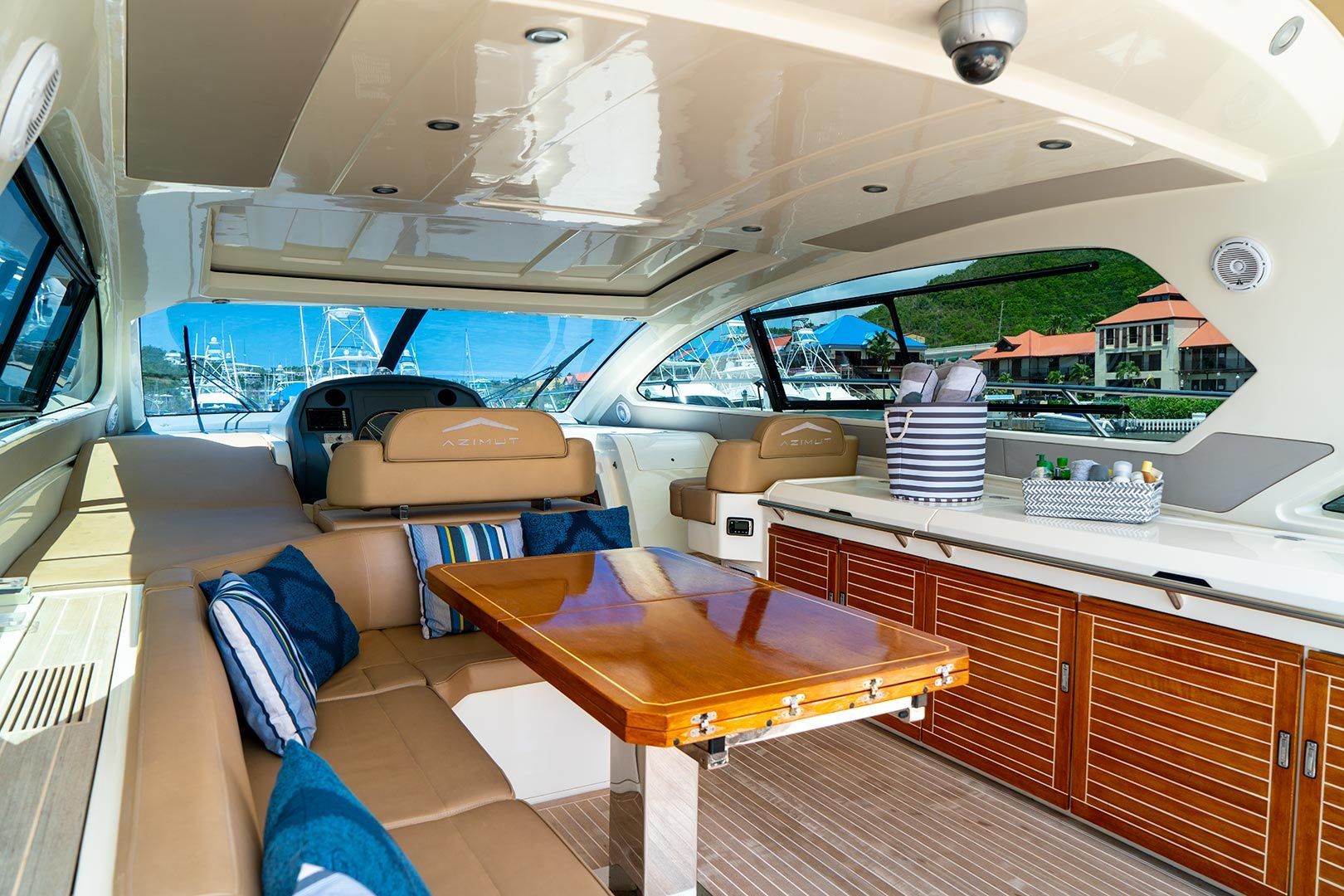 Interior of a luxury yacht with seating, a table, and kitchen area, overlooking water.