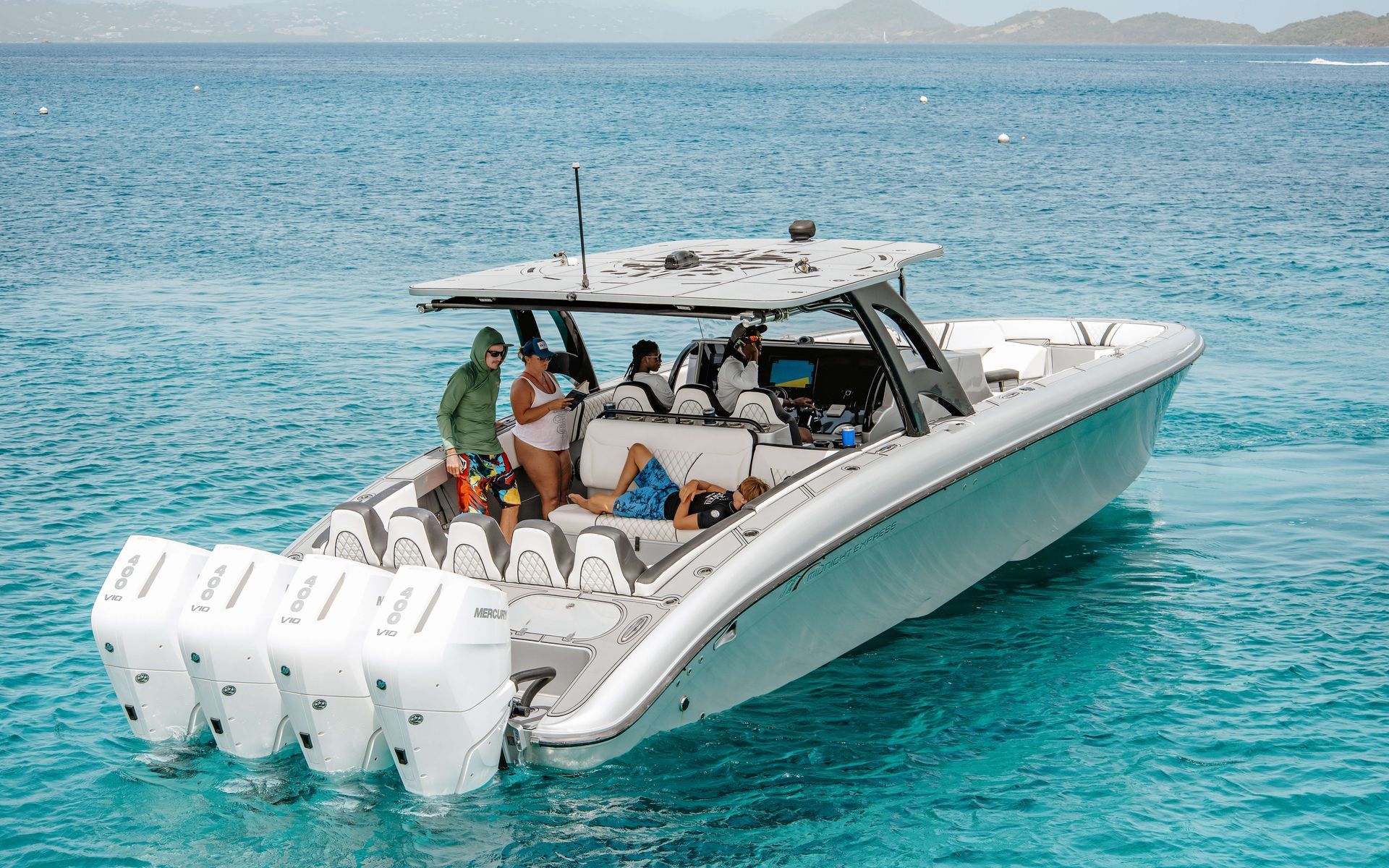 Large white powerboat with five outboard motors on turquoise water, people on board.
