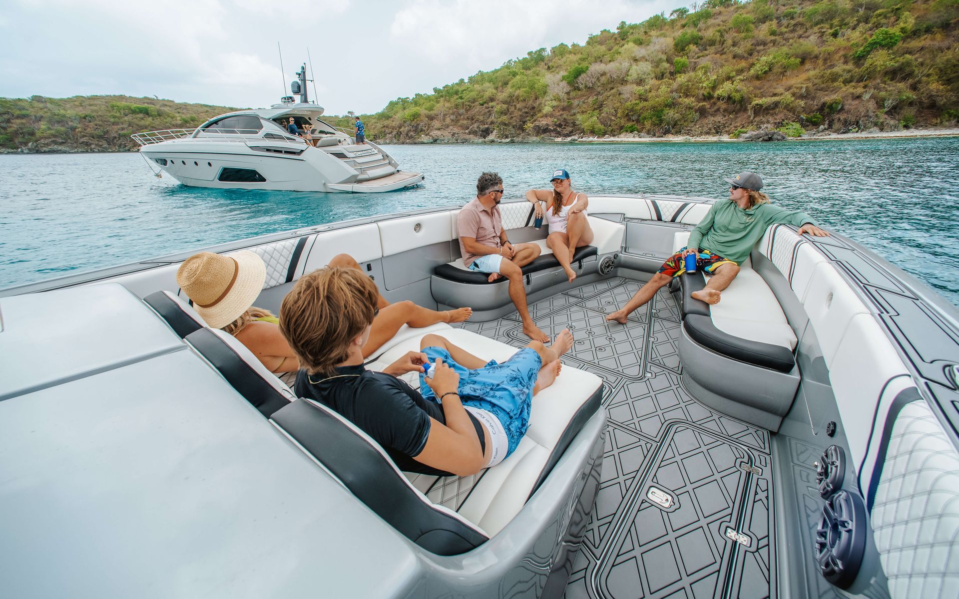 People lounging on a boat in a cove with a yacht in the background. Sunny day.