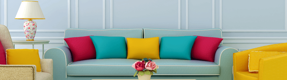 Red, turquoise and yellow cushions on an aqua sofa, next to a bright yellow tub chair, in front of pink roses in a pot on a coffee table
