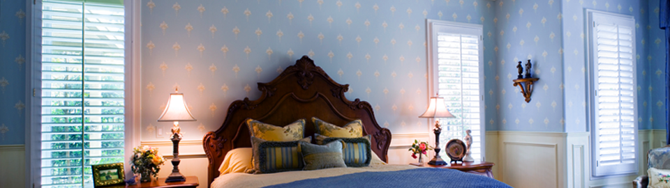 A bed with ornate timber bedhead, against a pale blue and white patterned wall, flanked by bedside tables with illuminated lamps